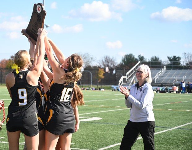 Mt. Hebron coach Jeannette Ireland watches as her players raise the championship trophy following their win over Northern Calvert during the Class 3A state field hockey championship at Paint Branch High School on Saturday, November 11, 2023.